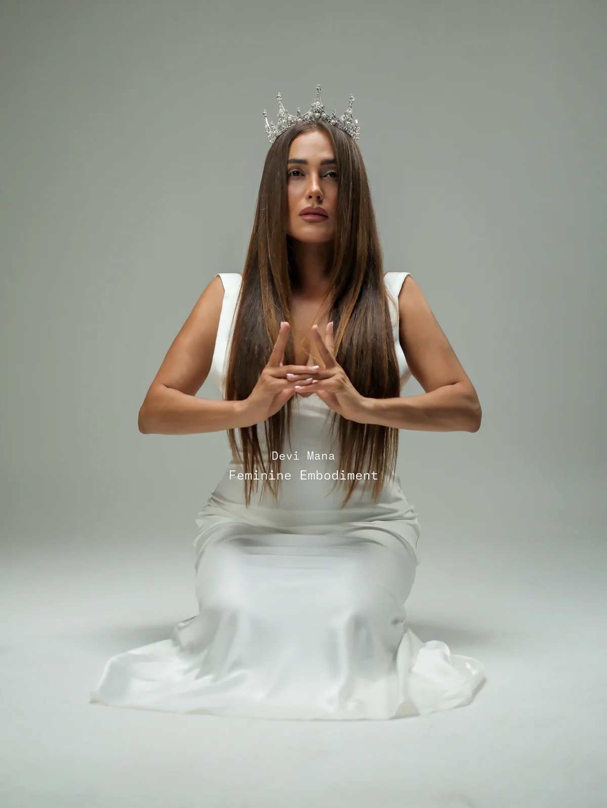 Devi Mana seated in a white dress, hands held together